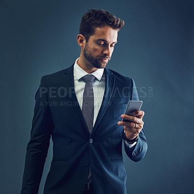 Buy stock photo Studio shot of a handsome young businessman using a cellphone against a dark background