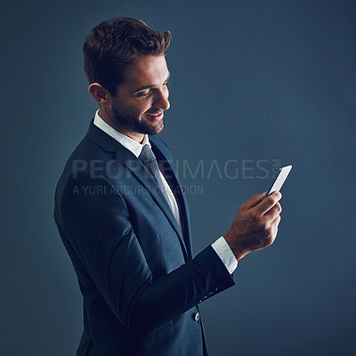Buy stock photo Studio shot of a handsome young businessman using a cellphone against a dark background