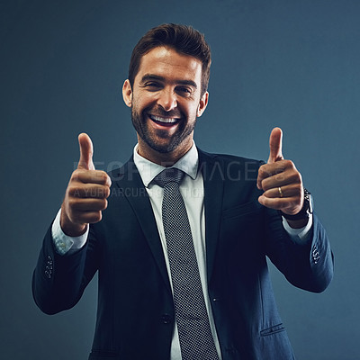Buy stock photo Studio portrait of a handsome young businessman showing thumbs up against a dark background