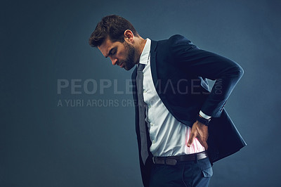 Buy stock photo Studio shot of a handsome young businessman suffering with back pain against a dark background