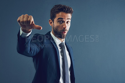 Buy stock photo Studio portrait of a handsome young businessman showing thumbs down against a dark background