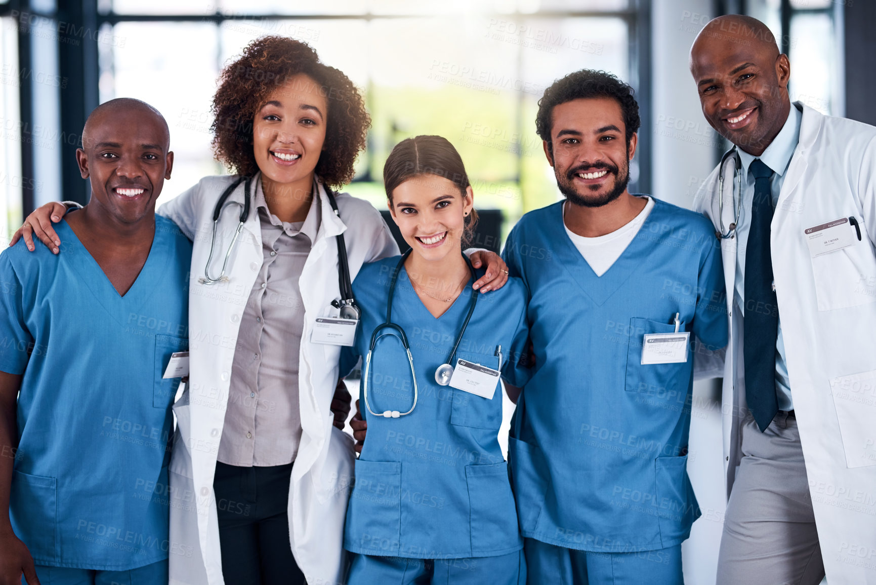 Buy stock photo Portrait of a cheerful group of doctors standing with their arms around each other inside of a hospital during the day