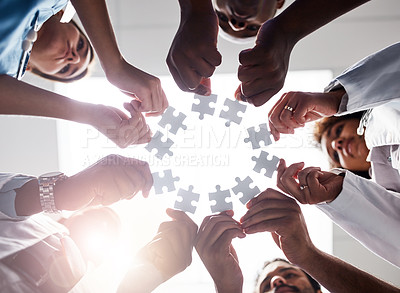 Buy stock photo Low angle shot of a group of doctors forming a huddle while each holds a puzzle piece inside of a hospital