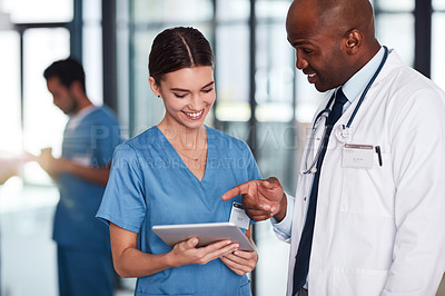 Buy stock photo Shot of two cheerful young doctors having a discussion over a digital tablet inside of a hospital