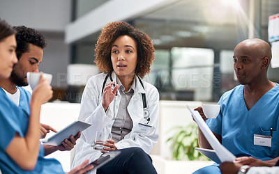 Buy stock photo Shot of a group of young doctors having a meeting over coffee at a table inside of a hospital during the day