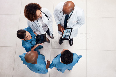Buy stock photo High angle shot of a group of young doctors having a discussion over a digital tablet inside of a hospital