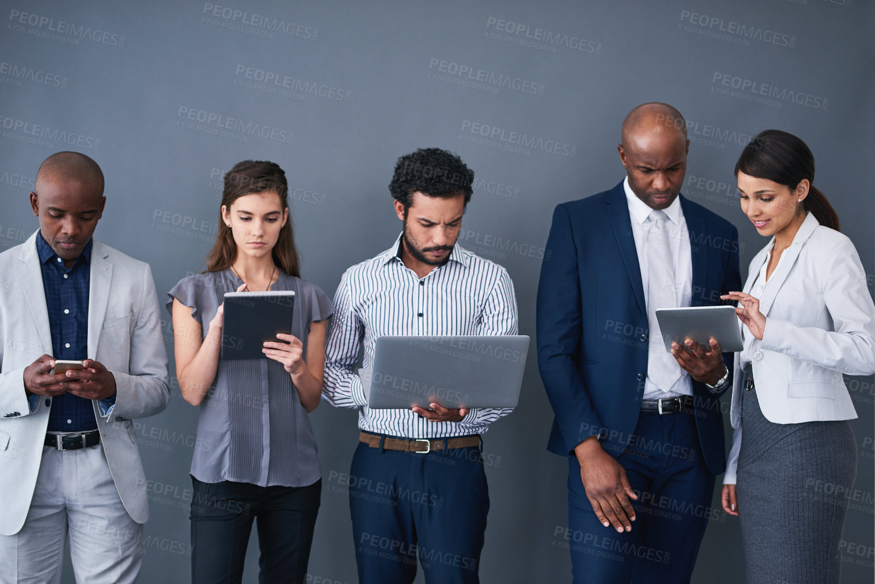 Buy stock photo Studio shot of a group of corporate businesspeople using different devices against a gray background