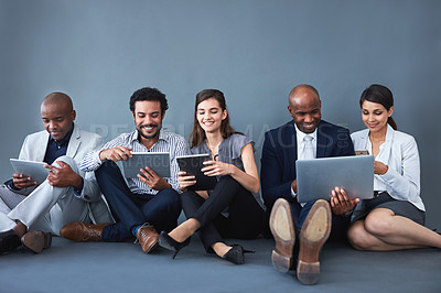 Buy stock photo Studio shot of a group of corporate businesspeople using different devices against a gray background