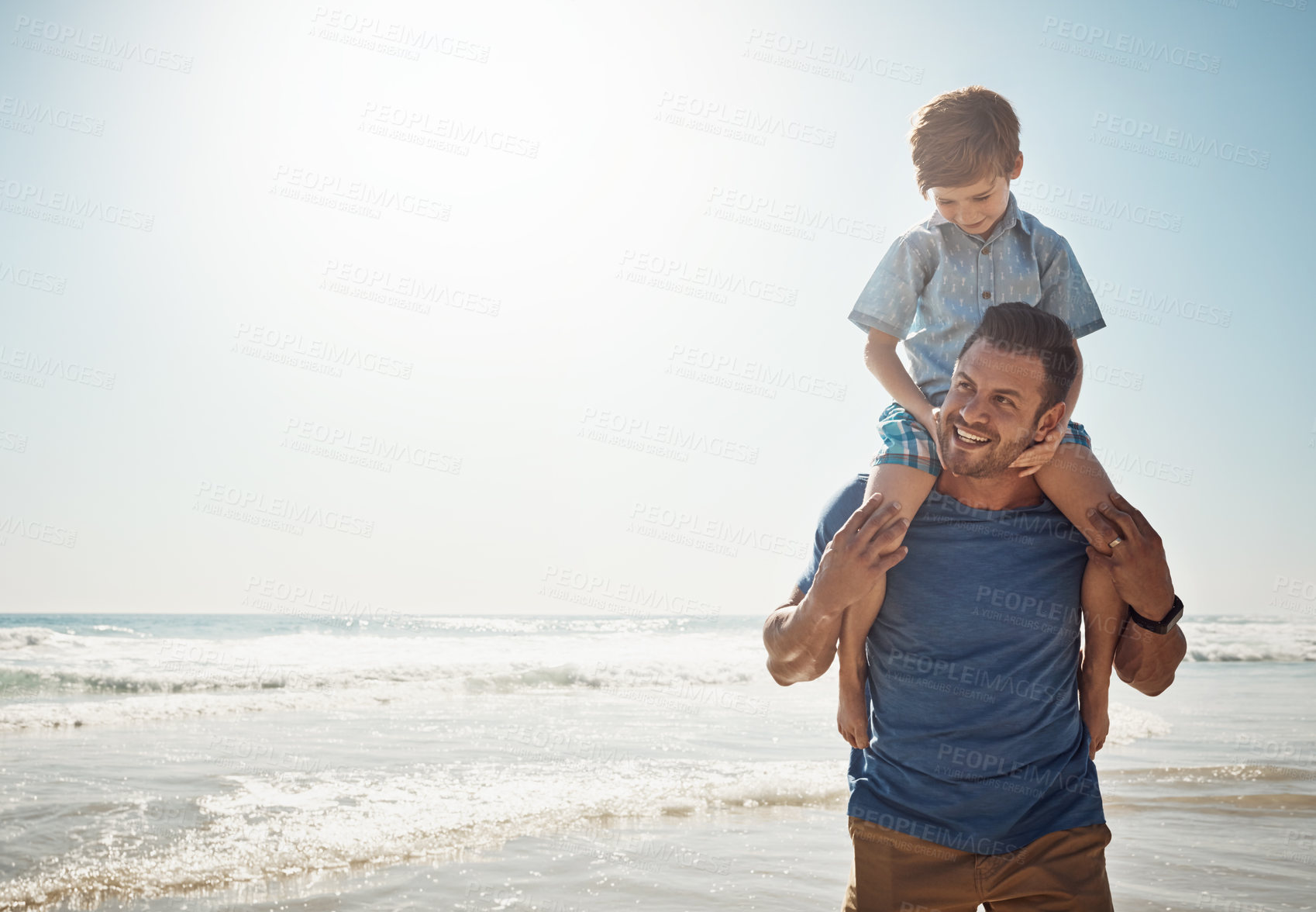 Buy stock photo Shot of a father carrying his little son on his shoulders at the beach