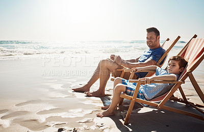Buy stock photo Shot of a father and his little son relaxing together on deck chairs at the beach
