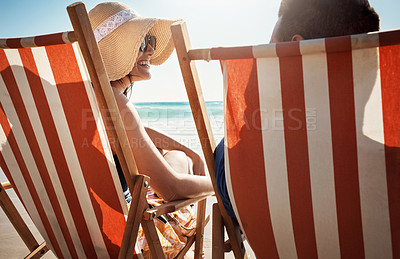 Buy stock photo Shot of a young couple relaxing on chairs at the beach