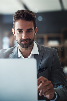 Buy stock photo Shot of a handsome young businessman using a laptop at his desk in a modern office