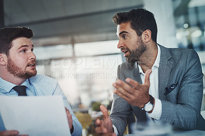 Buy stock photo Shot of two young businessmen going through paperwork together in a modern office