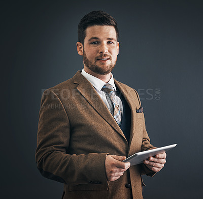 Buy stock photo Studio portrait of a handsome young businessman using a digital tablet against a dark background