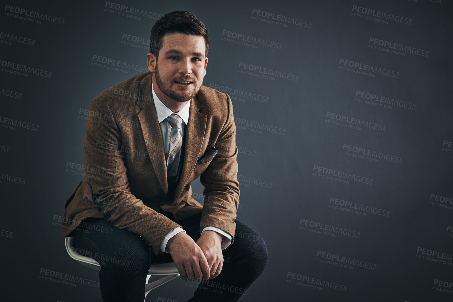 Buy stock photo Studio portrait of a handsome young businessman sitting on a chair against a dark background