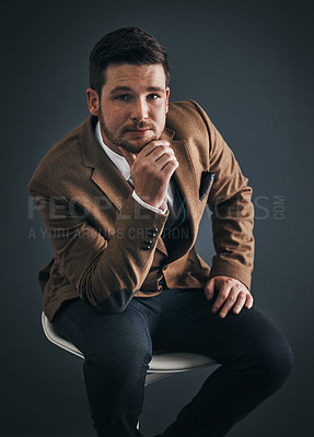 Buy stock photo Studio portrait of a handsome young businessman sitting on a chair against a dark background