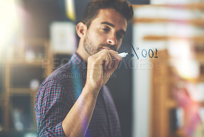 Buy stock photo Shot of a handsome young businessman writing notes on a glass wall in an office