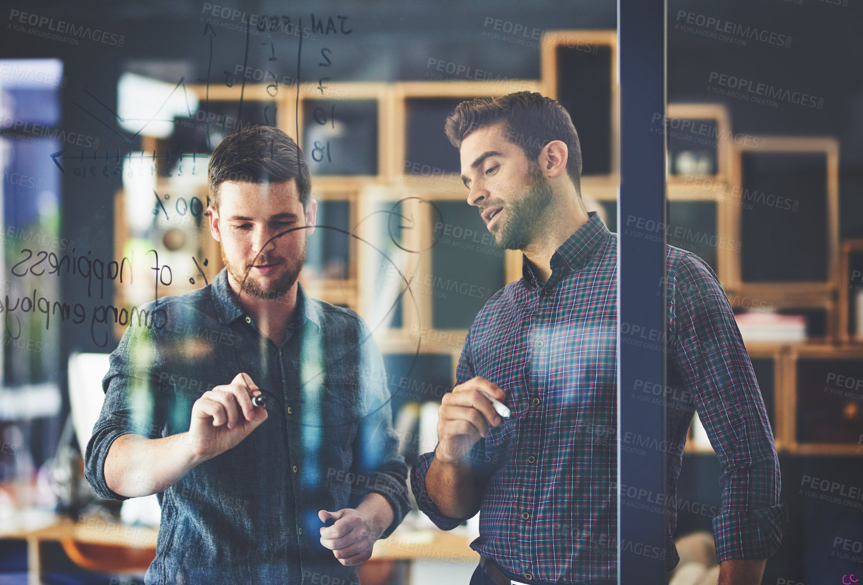 Buy stock photo Shot of two young businessmen brainstorming on a glass wall in an office