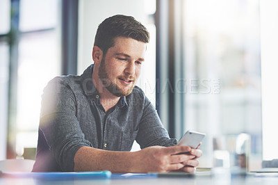Buy stock photo Shot of a young businessman using a cellphone in an office