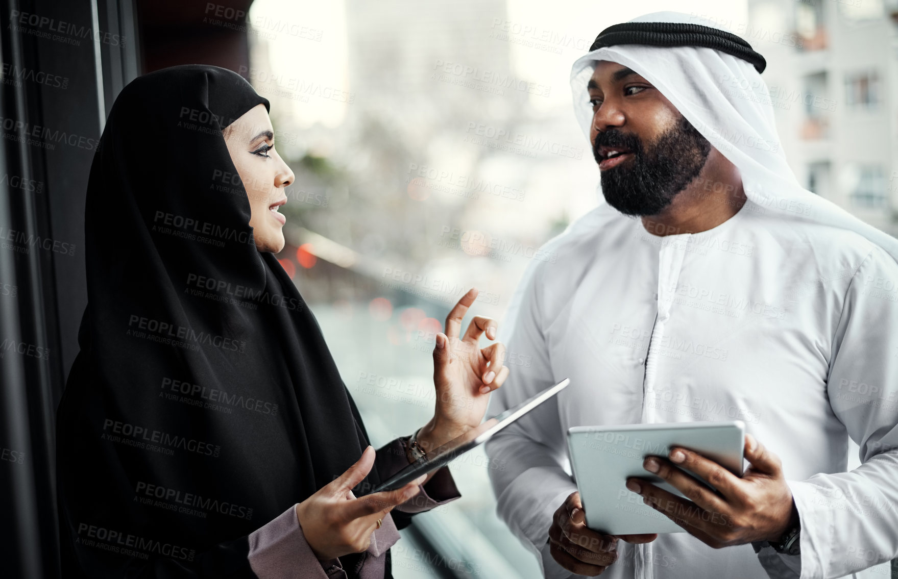 Buy stock photo Cropped shot of two young businesspeople dressed in Islamic traditional clothing using their tablets on the office balcony