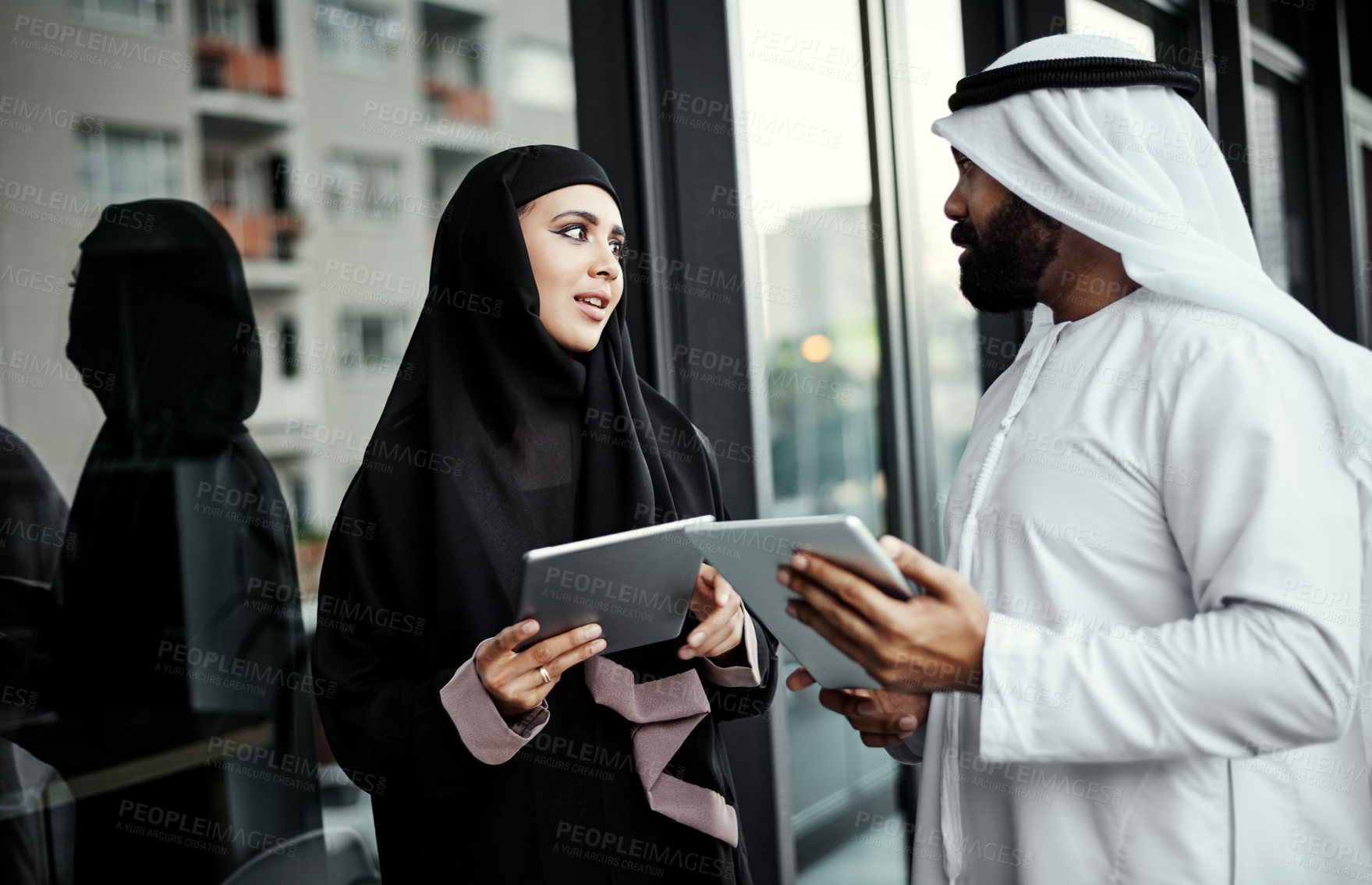 Buy stock photo Cropped shot of two young businesspeople dressed in Islamic traditional clothing using their tablets on the office balcony