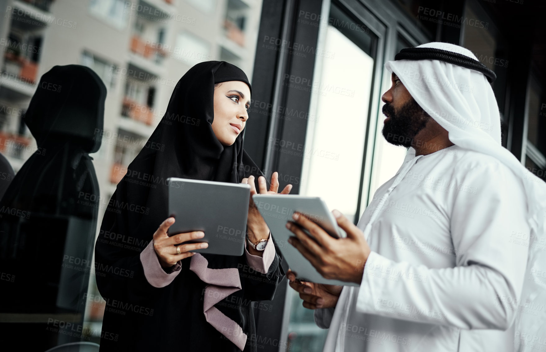 Buy stock photo Cropped shot of two young businesspeople dressed in Islamic traditional clothing using their tablets on the office balcony