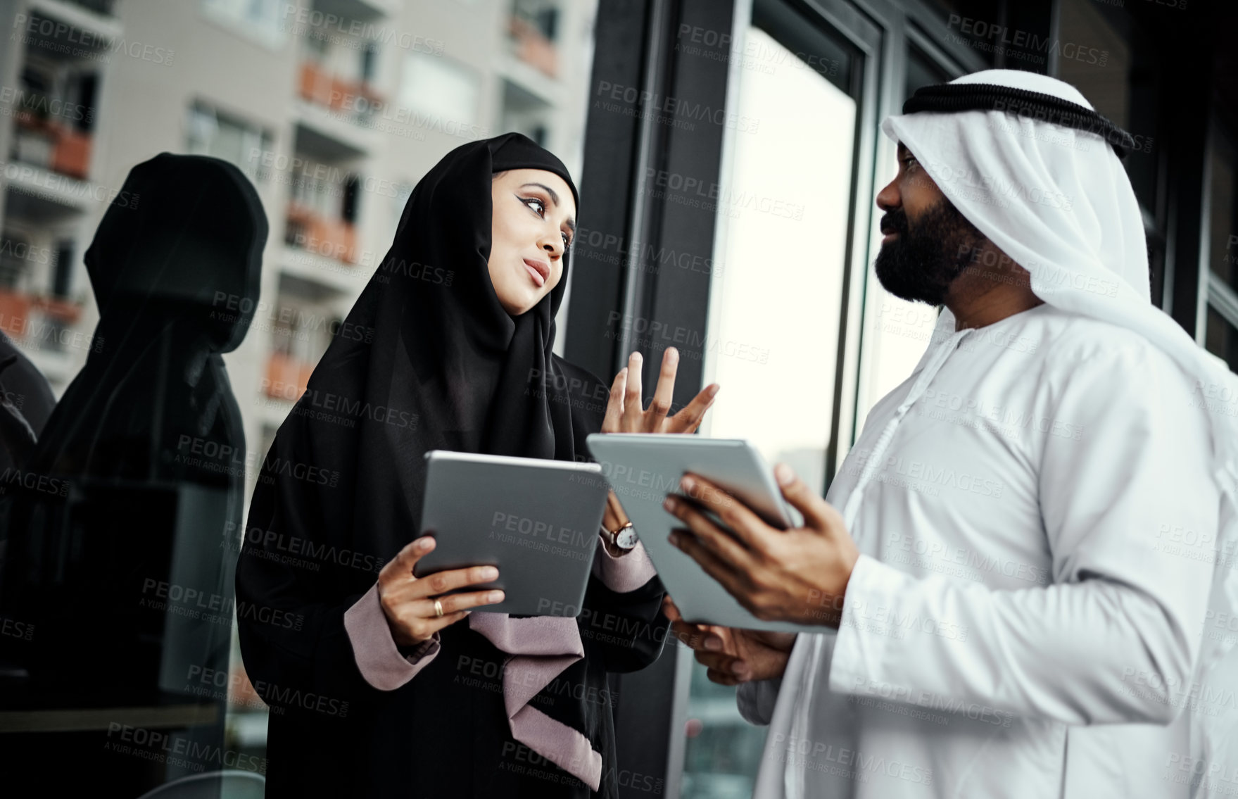 Buy stock photo Cropped shot of two young businesspeople dressed in Islamic traditional clothing using their tablets on the office balcony