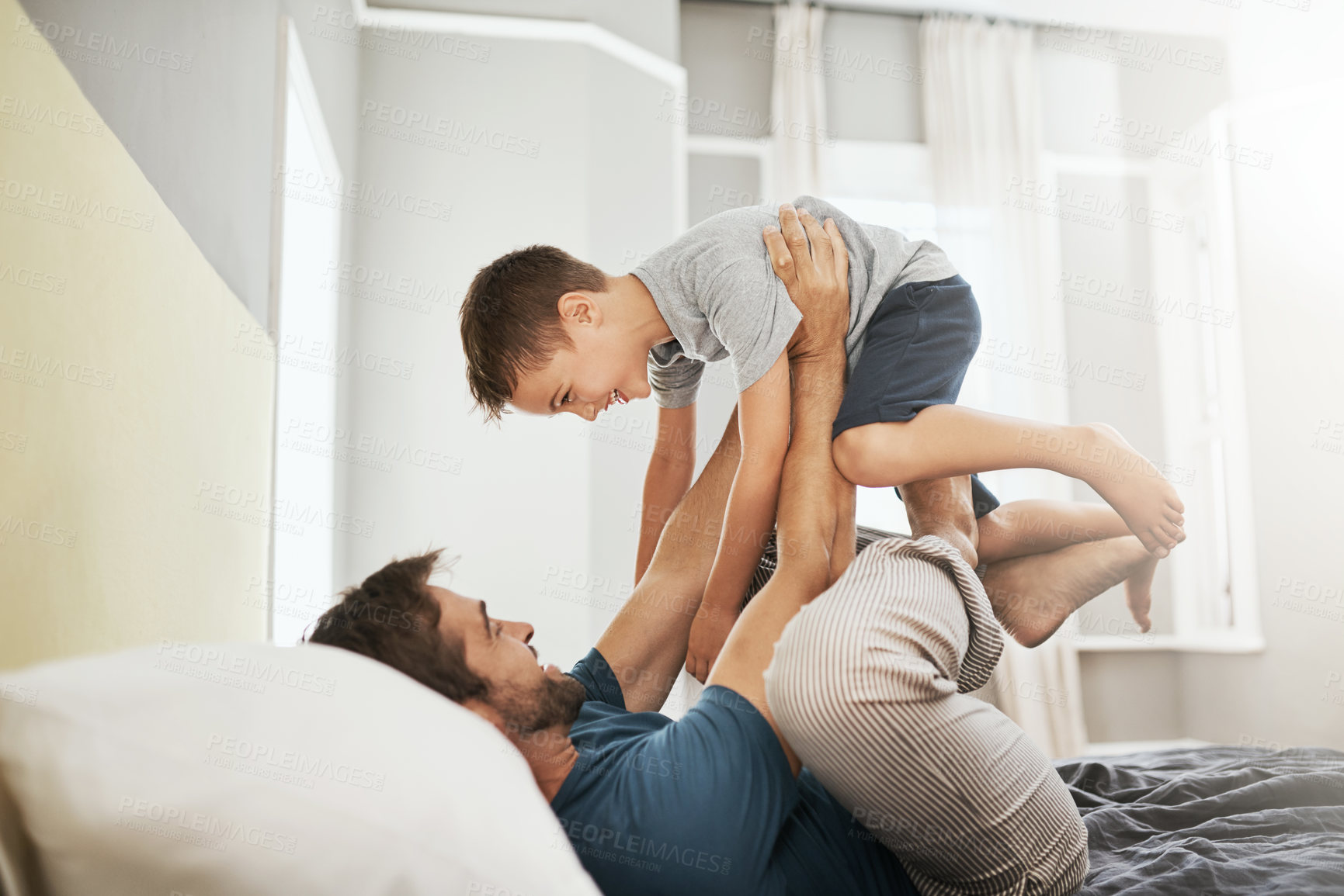 Buy stock photo Happy dad, bed and playing with son for bonding, care or support together in morning at home. Father with playful child, kid or little boy in air for fun day, weekend or holiday in bedroom at house