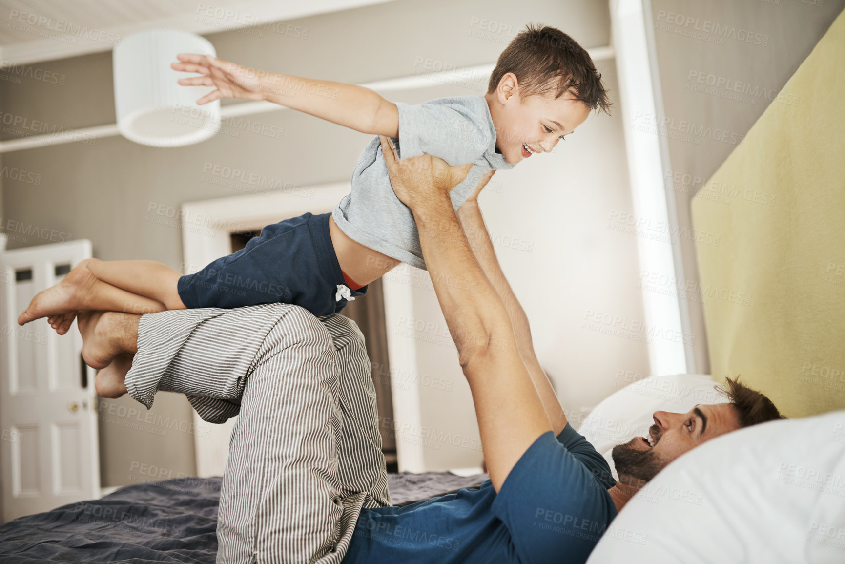 Buy stock photo Happy father, bed and playing with son for bonding, care or support together in morning at home. Dad with playful child, kid or little boy in air for fun day, weekend or holiday in bedroom at house