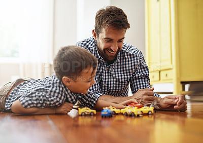 Buy stock photo Shot of a young boy and his father playing with cars on the floor