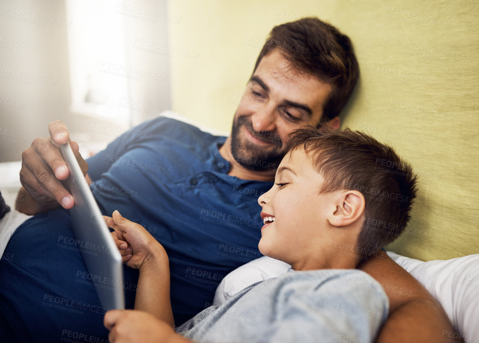 Buy stock photo Shot of a young man using a digital tablet with his son at home