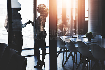 Buy stock photo Silhouetted shot of two businesspeople having a discussion in an office