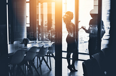 Buy stock photo Silhouetted shot of two businesspeople having a discussion in an office