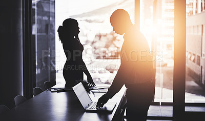 Buy stock photo Silhouetted shot of two businesspeople working in an office