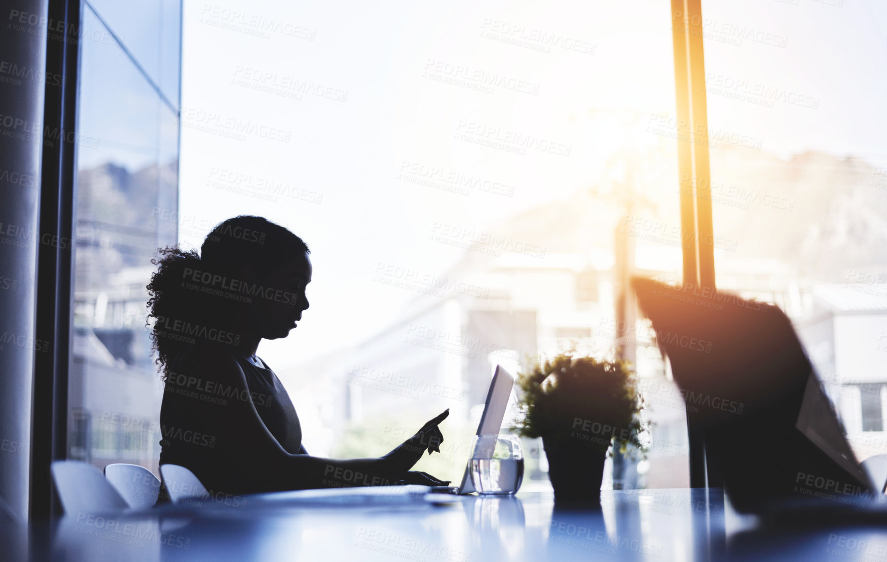 Buy stock photo Silhouetted shot of a young businesswoman working on a laptop in an office