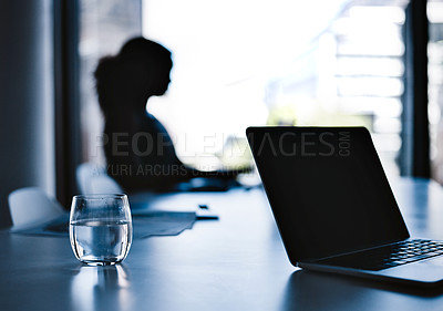 Buy stock photo Silhouetted shot of a young businesswoman working on a laptop in an office