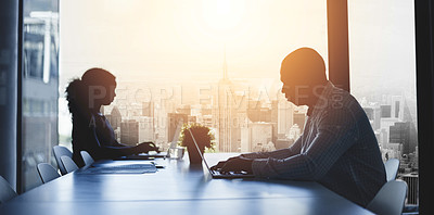 Buy stock photo Silhouetted shot of two businesspeople working in an office