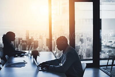 Buy stock photo Silhouette, working and sitting in the city office to focus in the morning. Business, people and typing at the boardroom table at a calm time of day. Cityscape, window and flare view of urban life.

