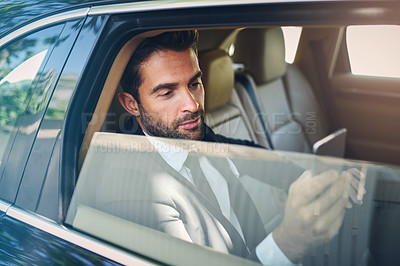 Buy stock photo Shot of a confident young businessman texting on his phone while being seated in the backseat of a car