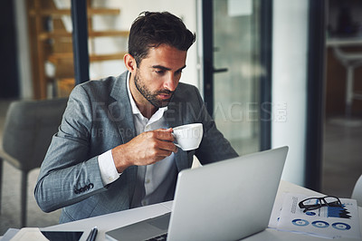 Buy stock photo Shot of a focused young businessman working on his laptop while drinking coffee inside of the office