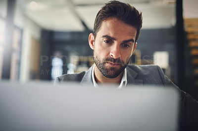 Buy stock photo Shot of a focused young businessman working on his laptop while contemplating inside of the office