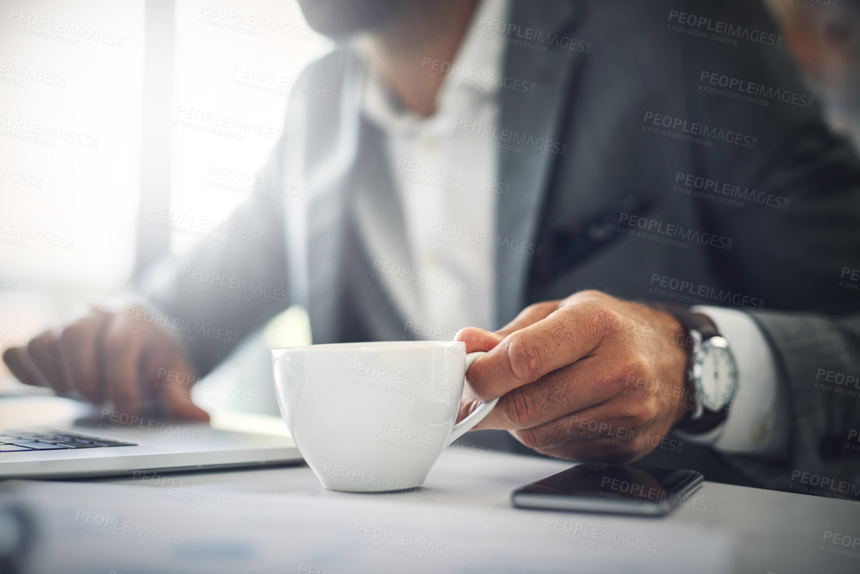 Buy stock photo Shot of an unrecognizable businessman working on his laptop while drinking coffee inside of the office