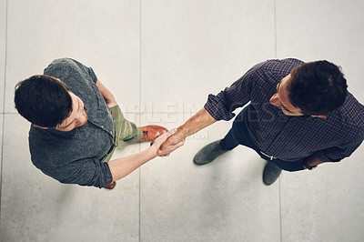 Buy stock photo High angle shot of two young businessmen shaking hands in agreement inside of the office during the day