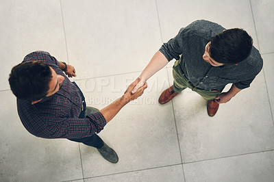 Buy stock photo High angle shot of two young businessmen shaking hands in agreement inside of the office during the day