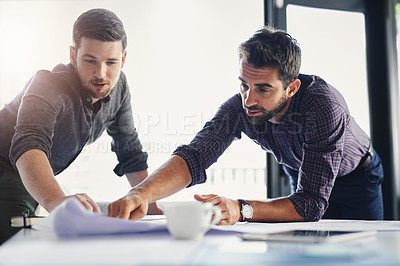 Buy stock photo Shot of two young businessmen working through business plans together inside of the office