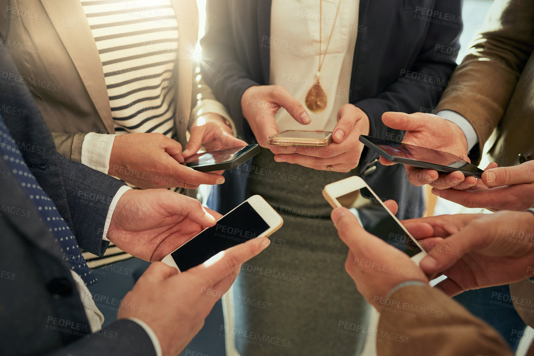 Buy stock photo Cropped shot of a group of businesspeople using their cellphones while standing in a huddle