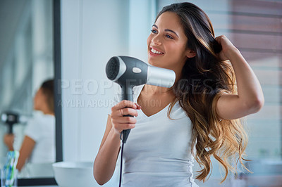 Buy stock photo Shot of an attractive young woman blowdrying her hair in the bathroom