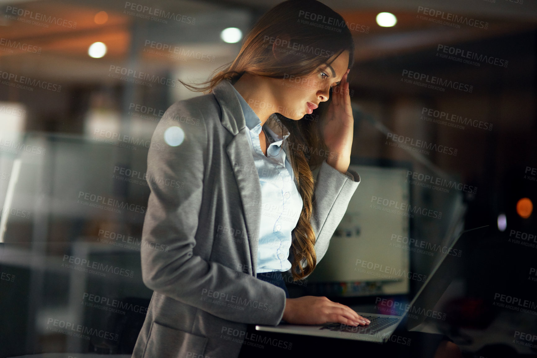 Buy stock photo Stressed, worried and tired female entrepreneur typing on a laptop and working overtime late at night. Frustrated and overworked young businesswoman with a headache doing a project with a deadline