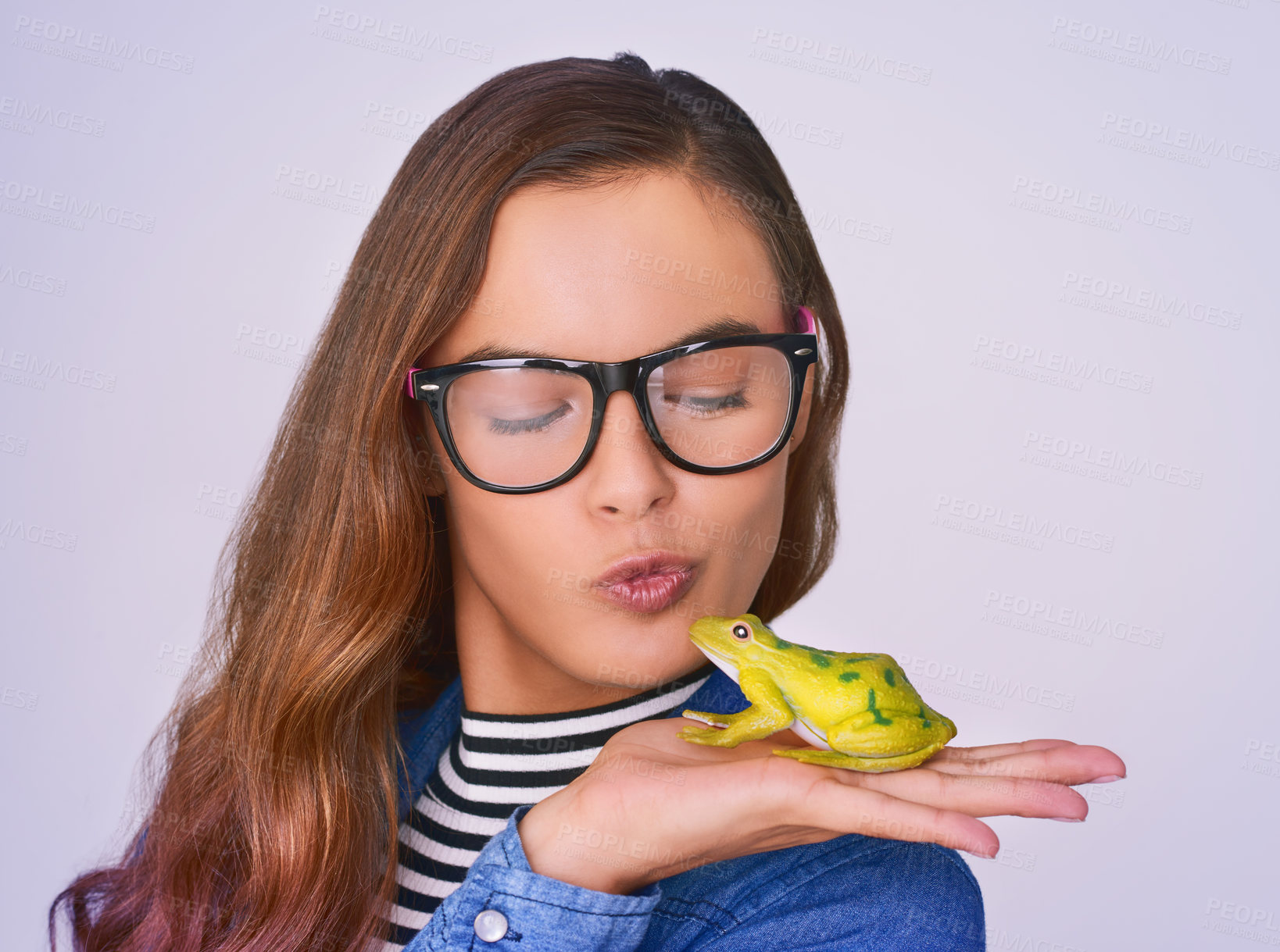 Buy stock photo Beauty, woman and kiss frog in studio for fairytale transformation, hope and romance fantasy with magic. Female, person, pout and comic with brand glasses, explore and wish on white background