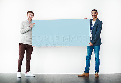 Buy stock photo Studio shot of two young men holding a blank placard against a white background